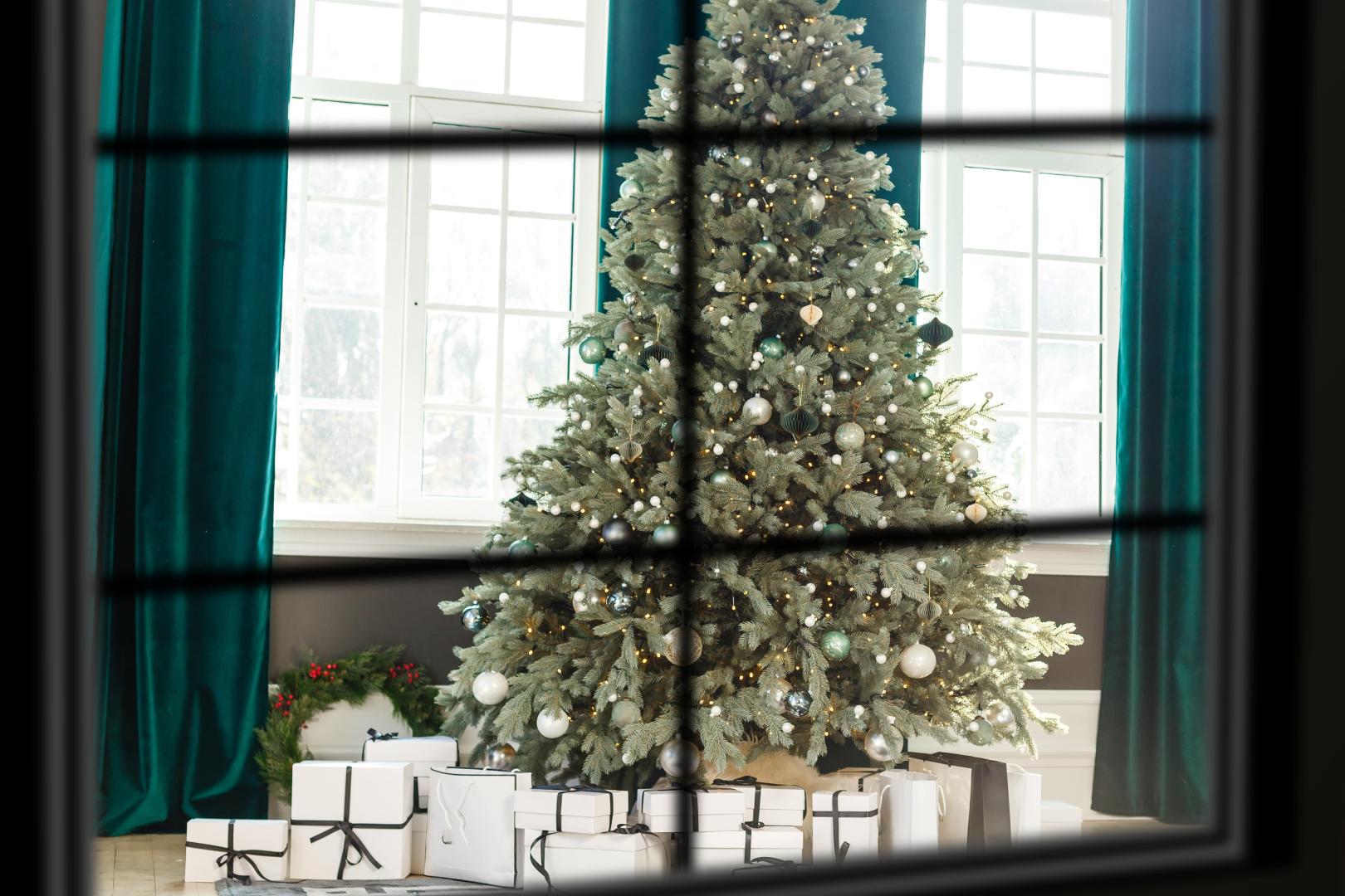 A view through a window with presents under a Christmas tree and green velvet curtains.