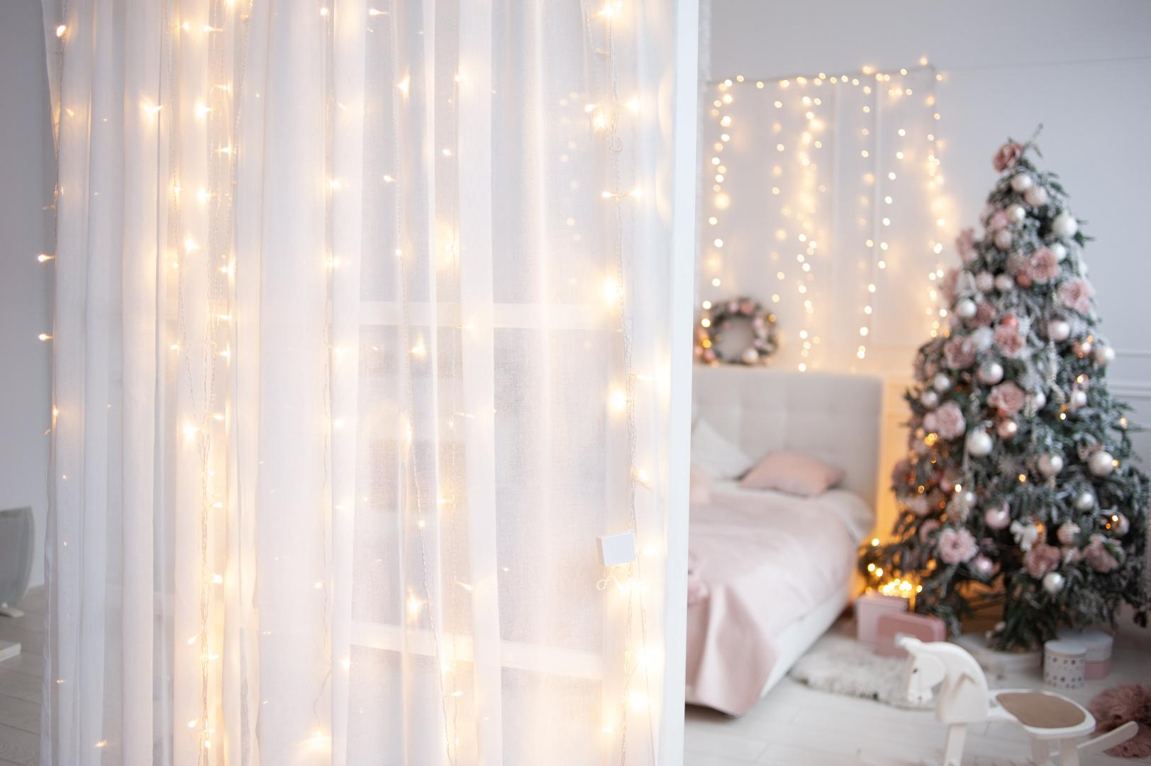 A bedroom decorated for Christmas in white and light pink tones.
