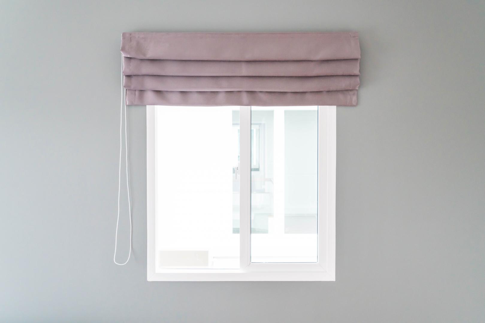 A white wall with a window with pink Roman shades.