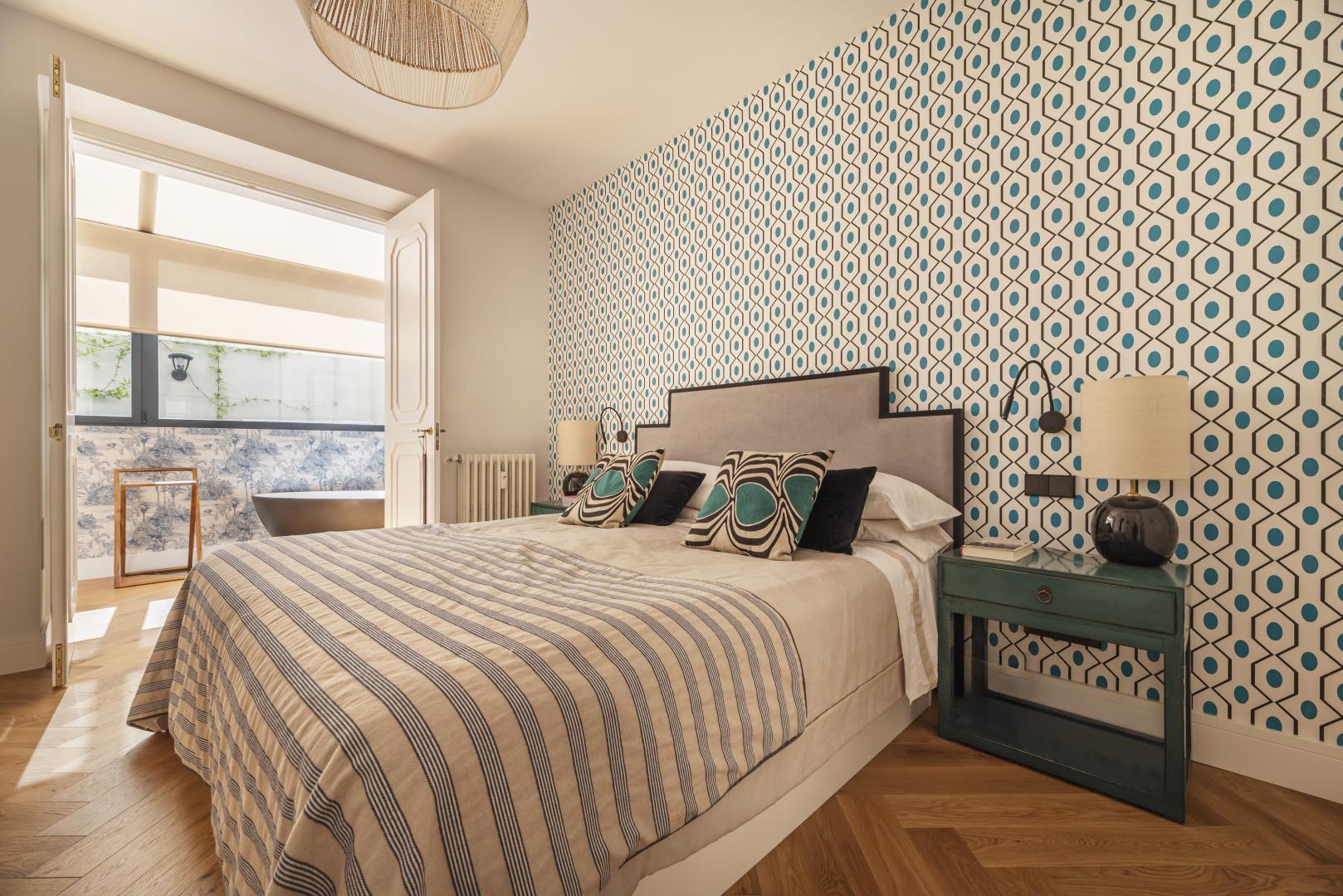 A bright bedroom with patterned wallpaper, bedding, and pillows.