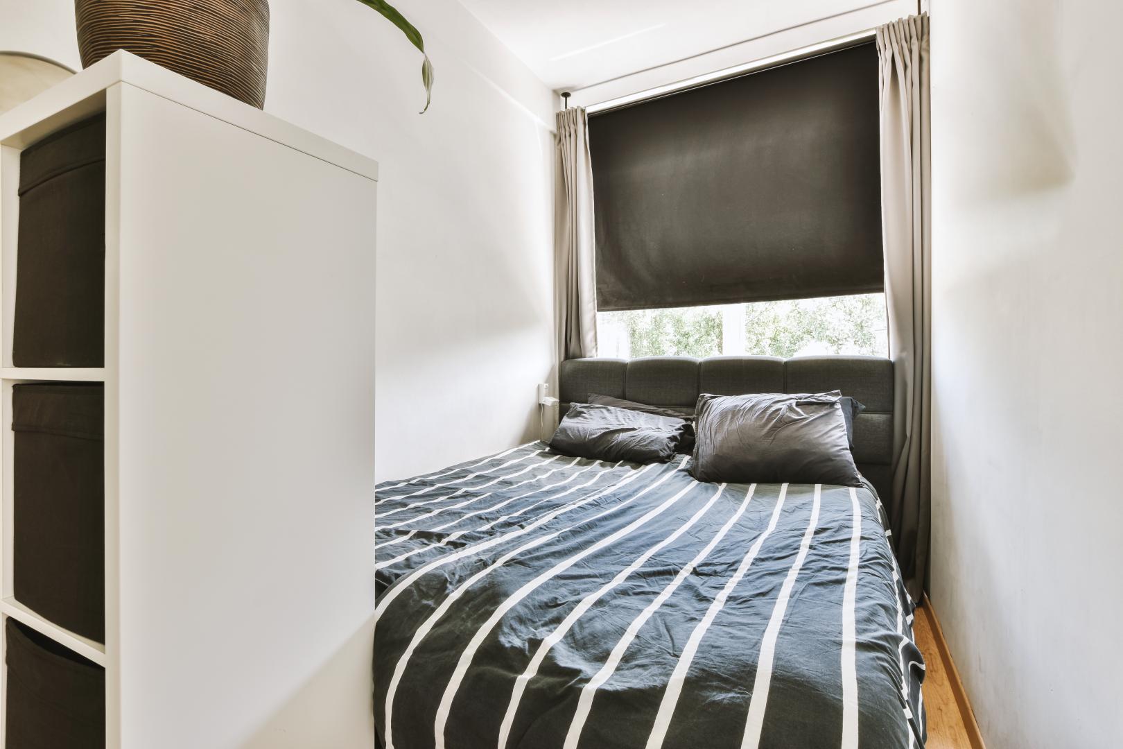 A small bedroom with shades layered with curtains.