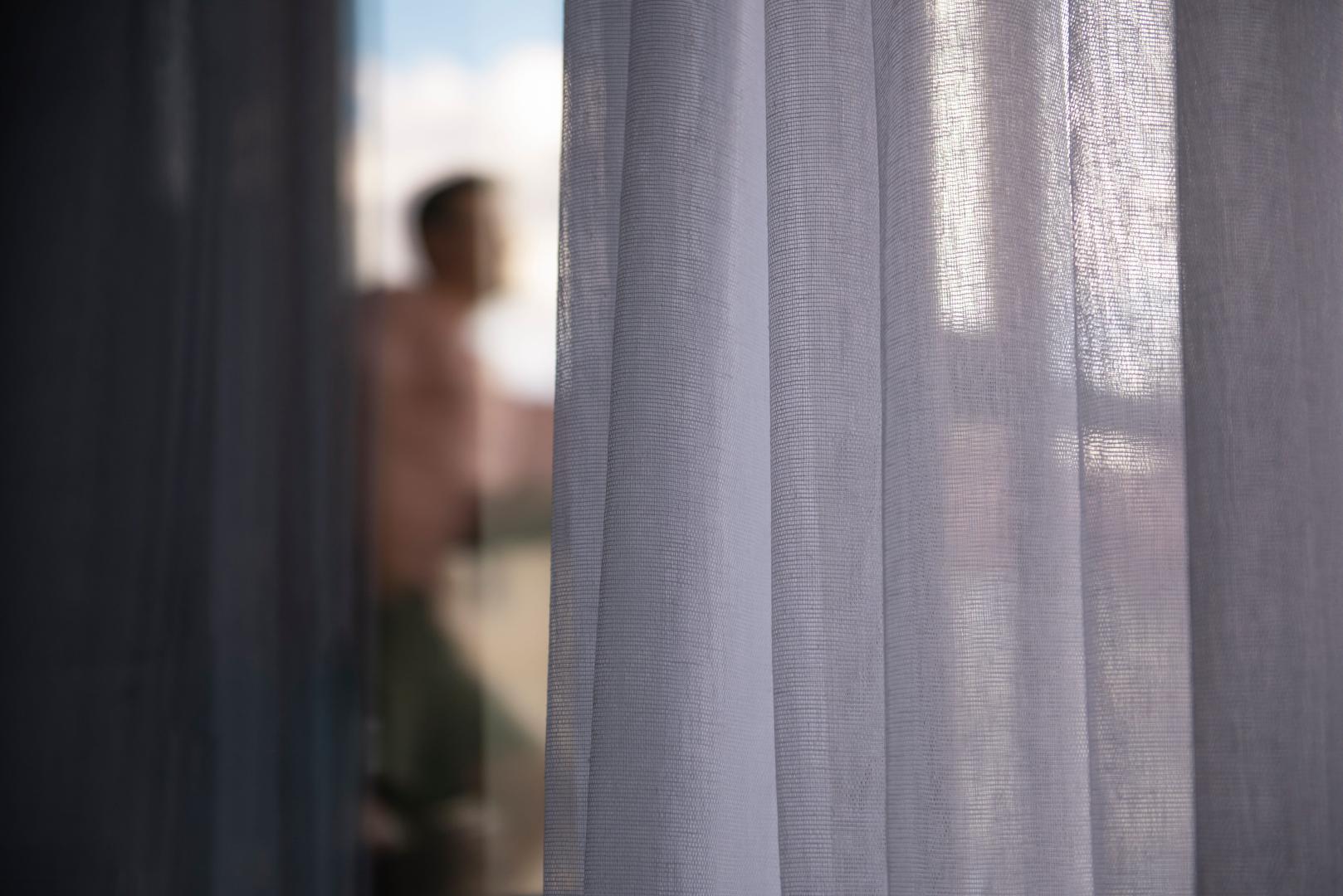 A close-up of white linen curtains and a man's silhouette in the distance.