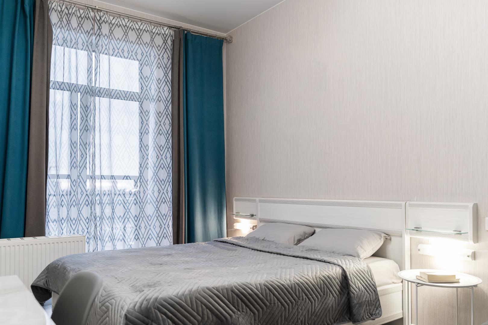 Modern bedroom interior with grey bed and teal curtains.