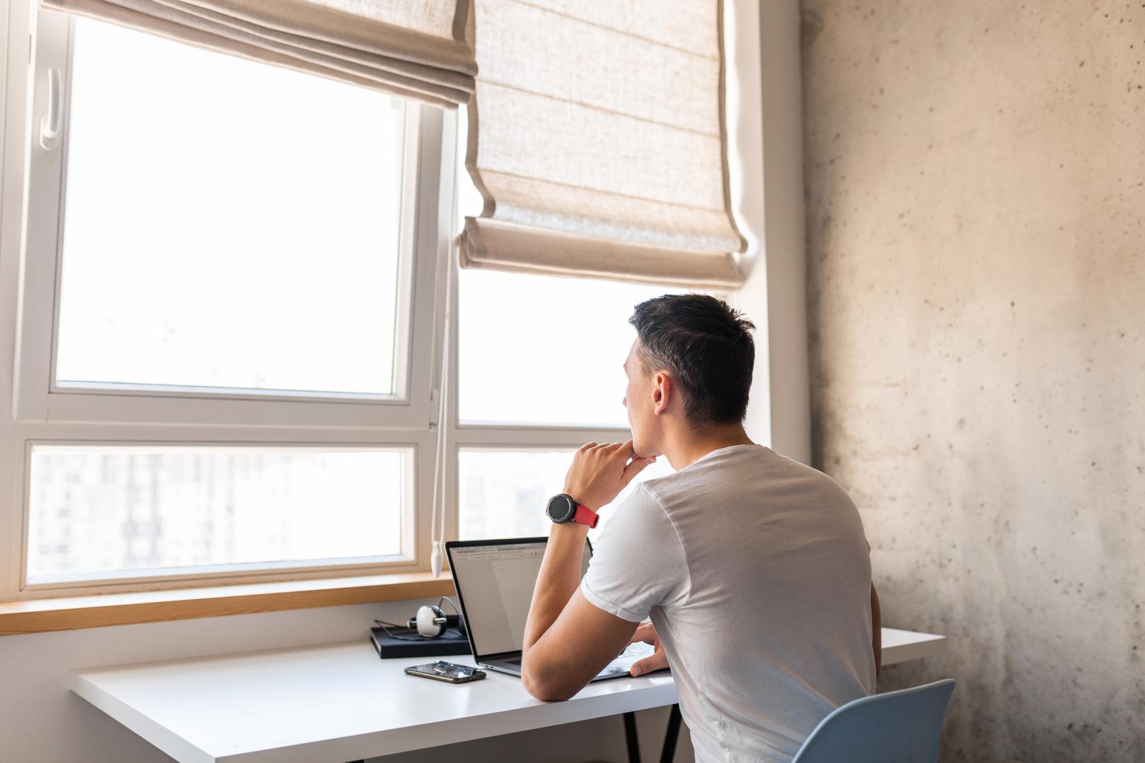 A man working by a window with light-colored Roman shades.