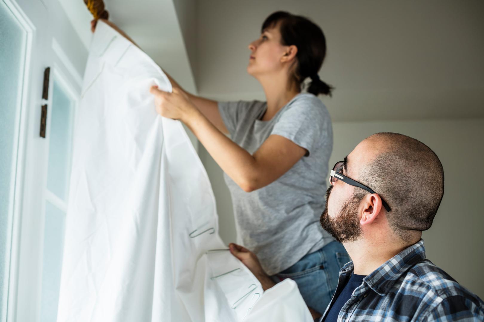 A couple installing white curtains.