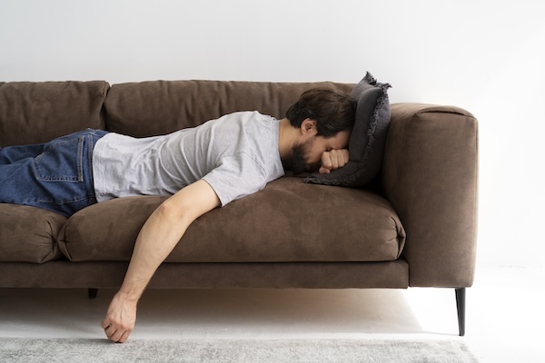 A man lying on a brown, worn-out couch.