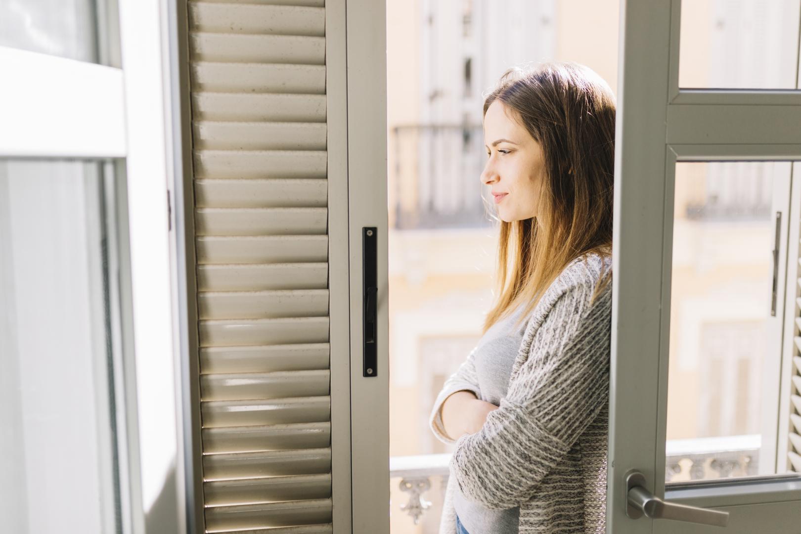 A woman standing on a balcony with shutters.