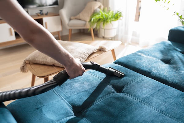 A person vacuuming a blue chenille couch.