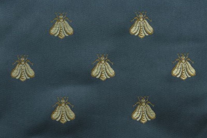 An insect print upholstery fabric with yellow embroidered bees on a dark blue background.