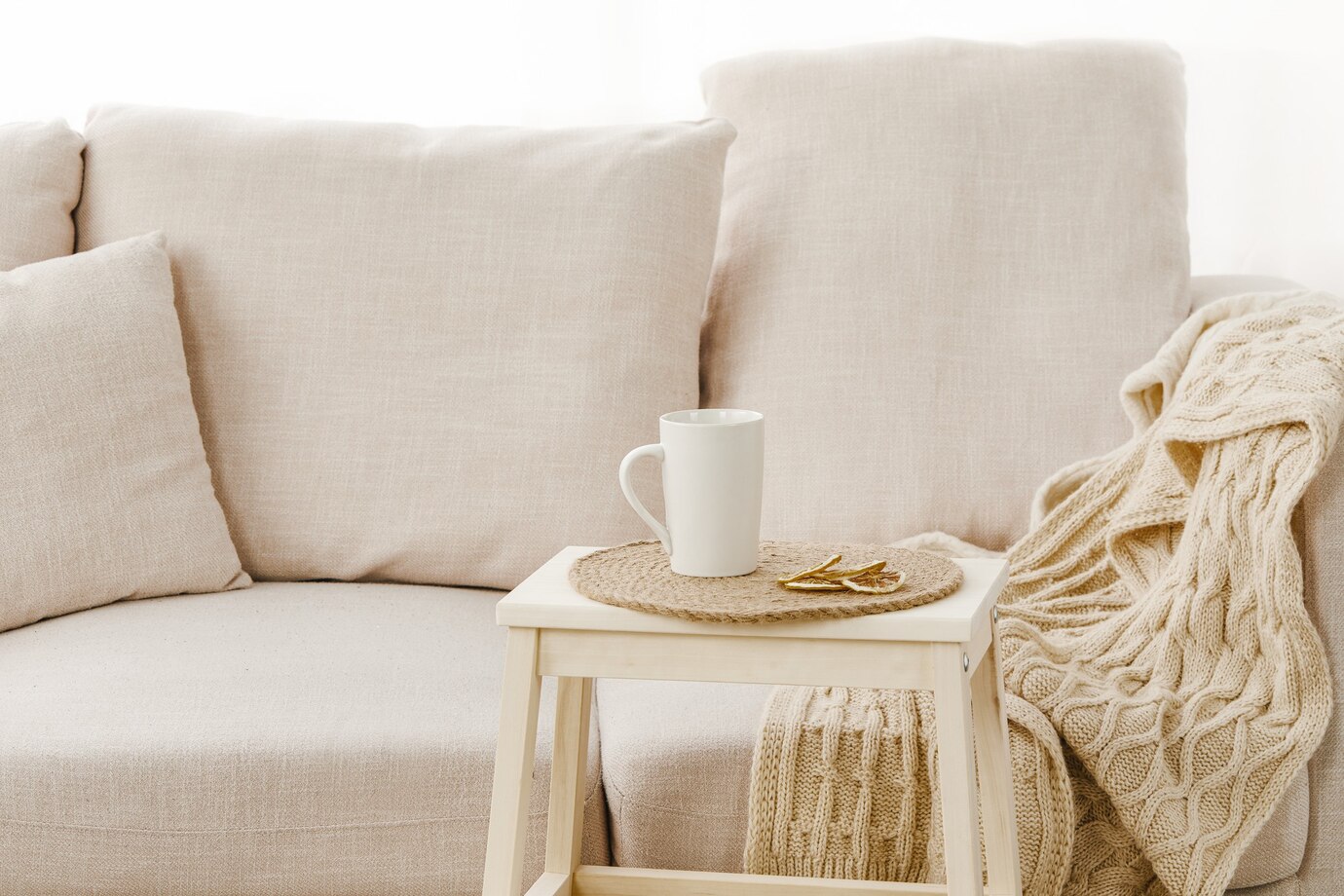 A white coffee cup placed on a small table adjacent to a bright linen couch.