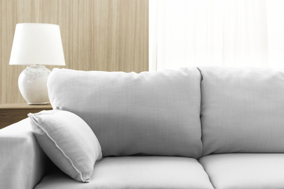 A light gray sofa in front of a white lamp and bright light shining through the window.