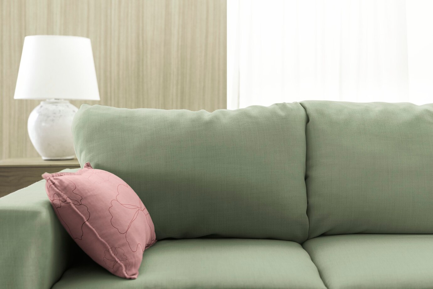 A green polyester couch with a pink throw pillow and a white lamp behind it.