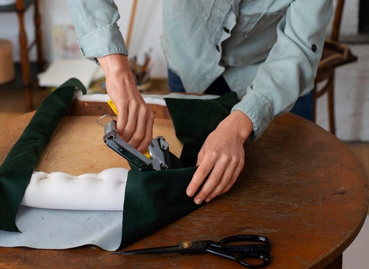 A woman stapling a green upholstery fabric on a chair seat.