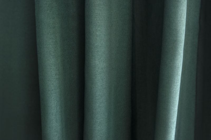 Closeup of a dark green polyester fabric with pleats.