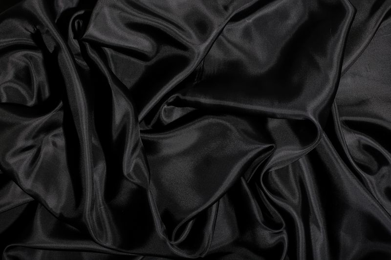 A luxurious black silk fabric background, highlighting its soft texture and glossy finish.