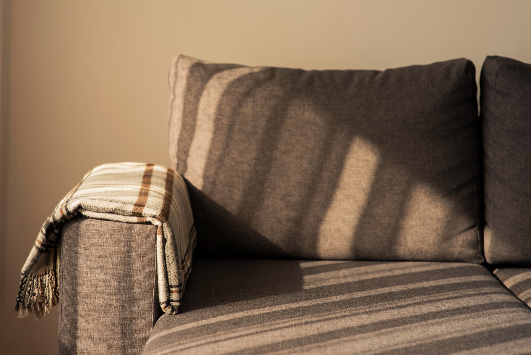 A gray canvas fabric couch with shadows falling on it.