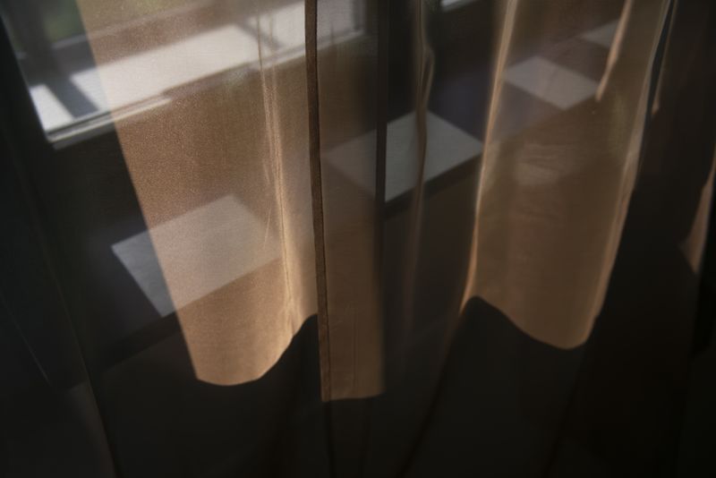 A sunlit window adorned with flowing voile fabric curtains, casting gentle light into the room.