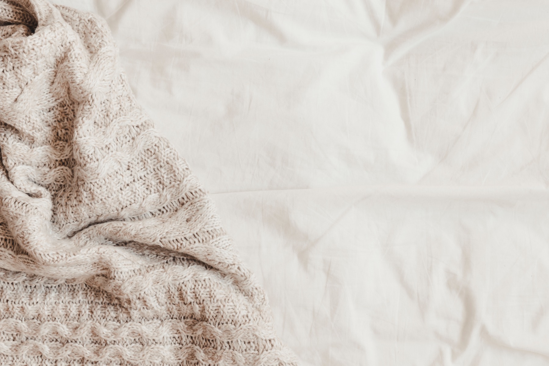 A cozy beige blanket draped over a white bed sheet.