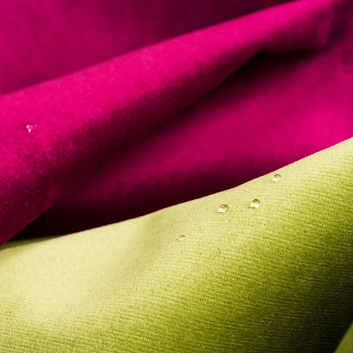 A close-up of colorful fabrics in bright green and pink, with a few droplets of water on them.